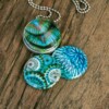 Roestvrij stalen fotomedaillon ketting in teal blauw met drie verschillende verwisselbare voorkanten met close up foto`s in pauw blauw.Pauwenveer close up. Rvs/roesvrij stalen fotomedaillon. Voor het dicht bij je dragen van je favoriete foto.