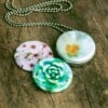 Roestvrij stalen fotomedaillon ketting met drie verschillende verwisselbare voorkanten met close up foto`s van roze witte en groene bloemen. Rvs/roesvrij stalen fotomedaillon. Voor het dicht bij je dragen van je favoriete foto.