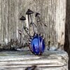 Handgemaakte paddenstoelenbroche met blauw glas en zwart gepatineerd koper