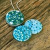 Fotomedaillon ketting met 3 verschillende verwisselbare voorkanten met foto`s van 3 verschillende dotting art kunstwerken.Blauw tinten dotting art.