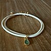 Stijlvol armbandje van crèmekleurig polyurethaan leer met een klein groen bedeltje.