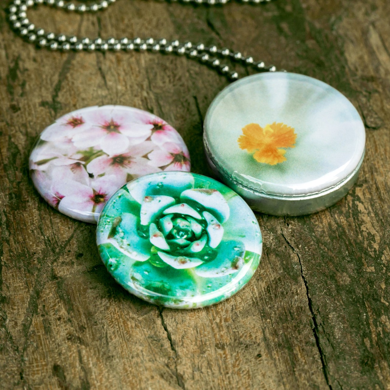 Roestvrij stalen fotomedaillon ketting met drie verschillende verwisselbare voorkanten met close up foto`s van roze witte en groene bloemen. Rvs/roesvrij stalen fotomedaillon. Voor het dicht bij je dragen van je favoriete foto.