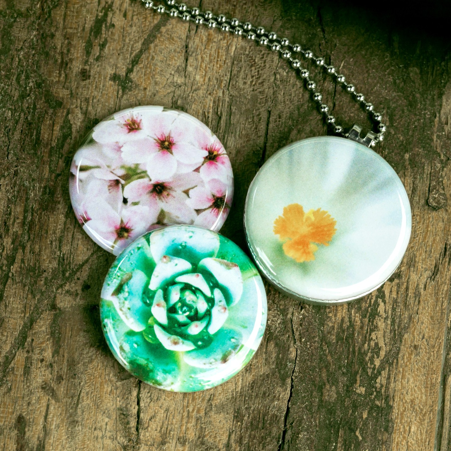 Roestvrij stalen fotomedaillon ketting met drie verschillende verwisselbare voorkanten met close up foto`s van roze witte en groene bloemen. Rvs/roesvrij stalen fotomedaillon. Voor het dicht bij je dragen van je favoriete foto.