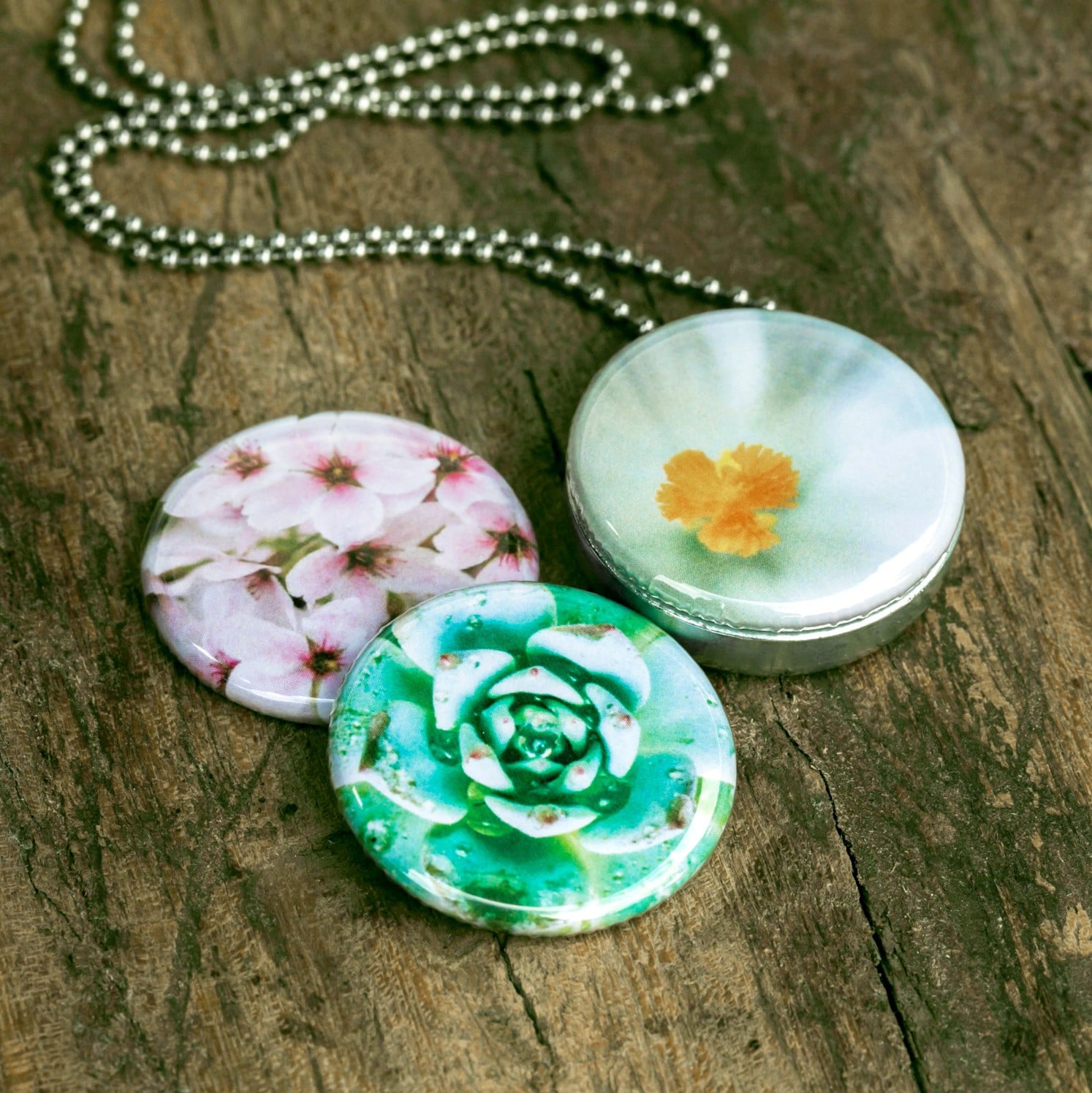 Roestvrij stalen fotomedaillon ketting met drie verschillende verwisselbare voorkanten met close up foto`s van roze witte en groene bloemen. Rvs/roesvrij stalen fotomedaillon. Voor het dicht bij je dragen van je favoriete foto.