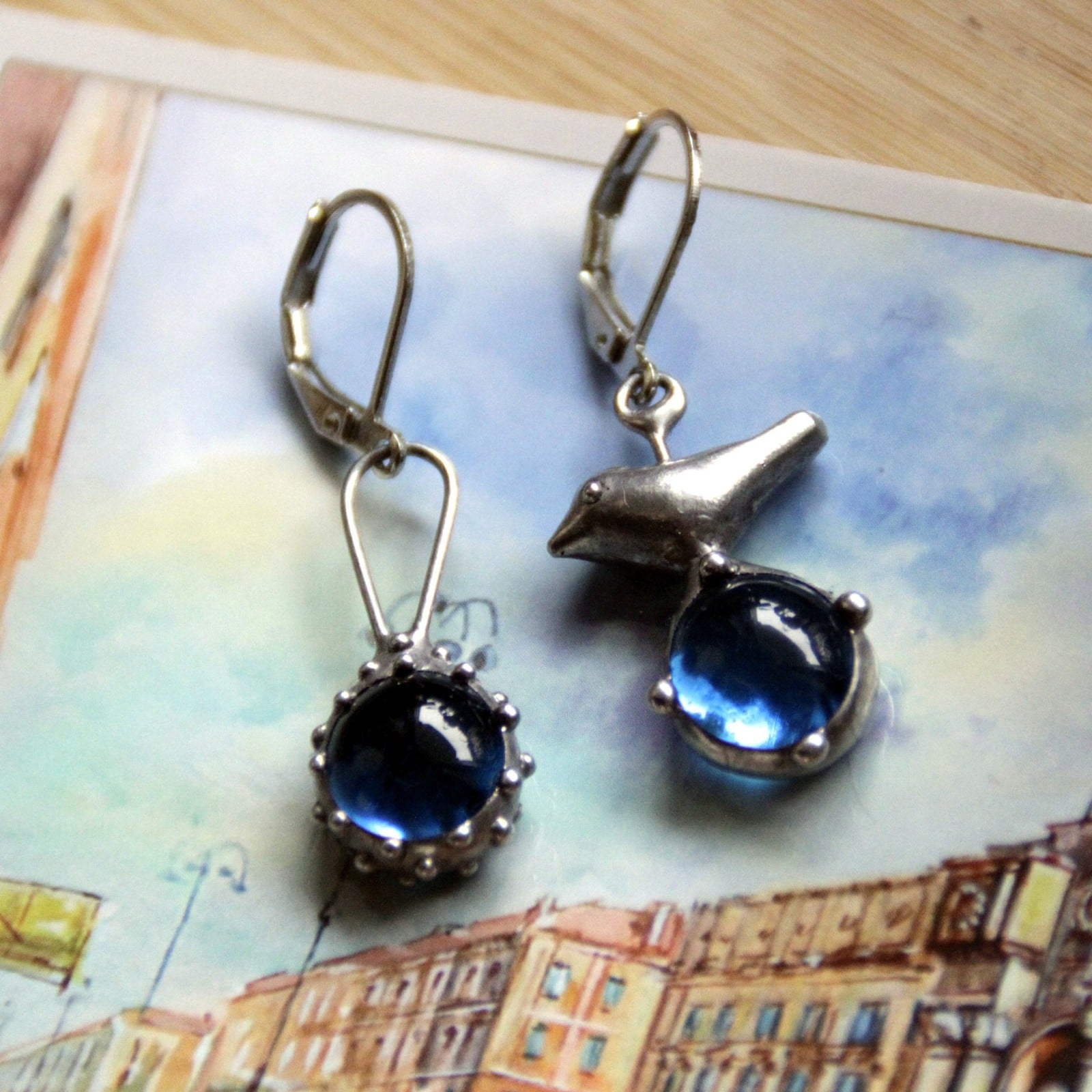 Asymmetrische handgemaakte vogeloorbellen met blauw glas en zilverkle… - 143146 Asymmetrische handgemaakte vogeloorbellen met blauw glas en zilverkleurig koper