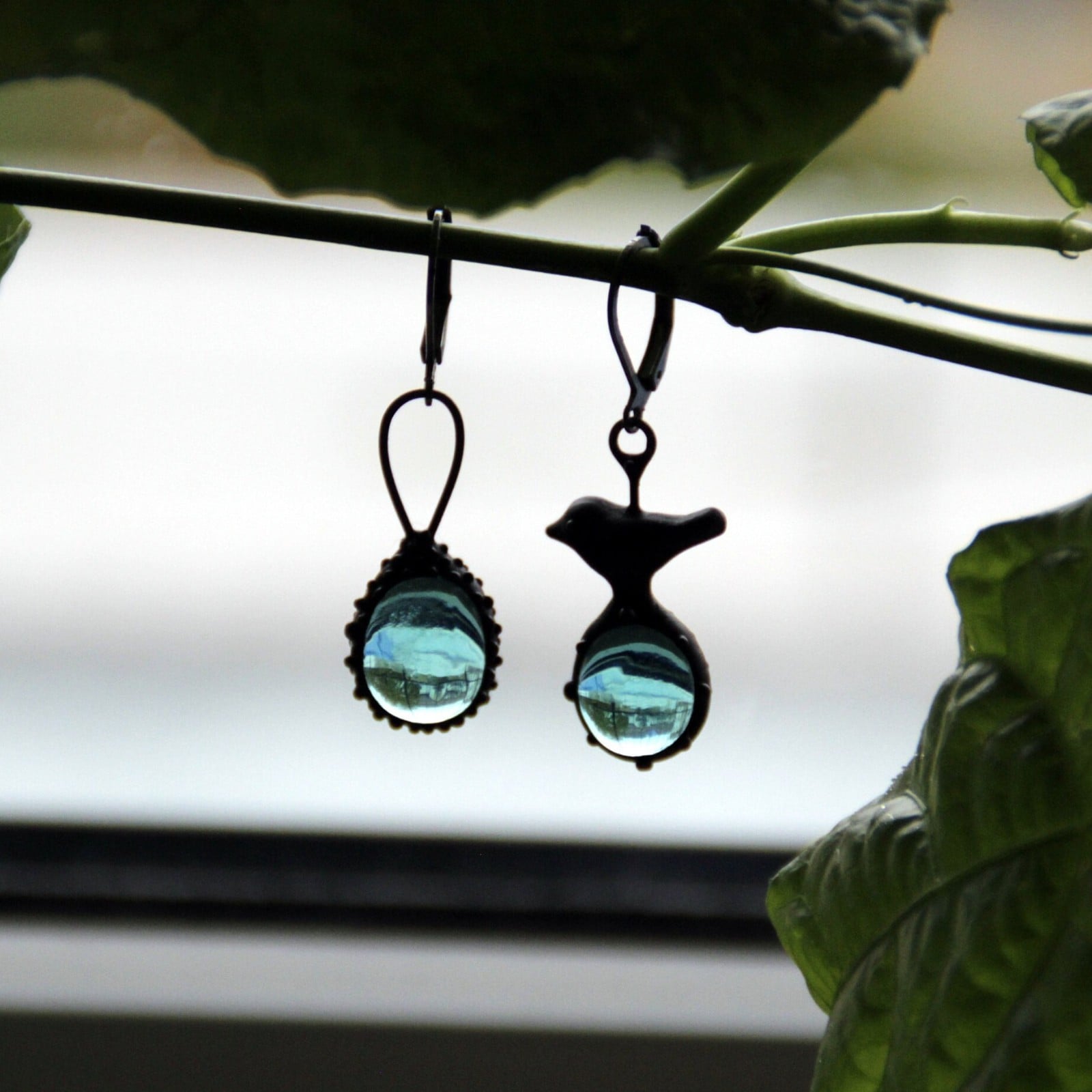 Asymmetrische handgemaakte vogeloorbellen met blauw glas en zwart gepatineerd koper