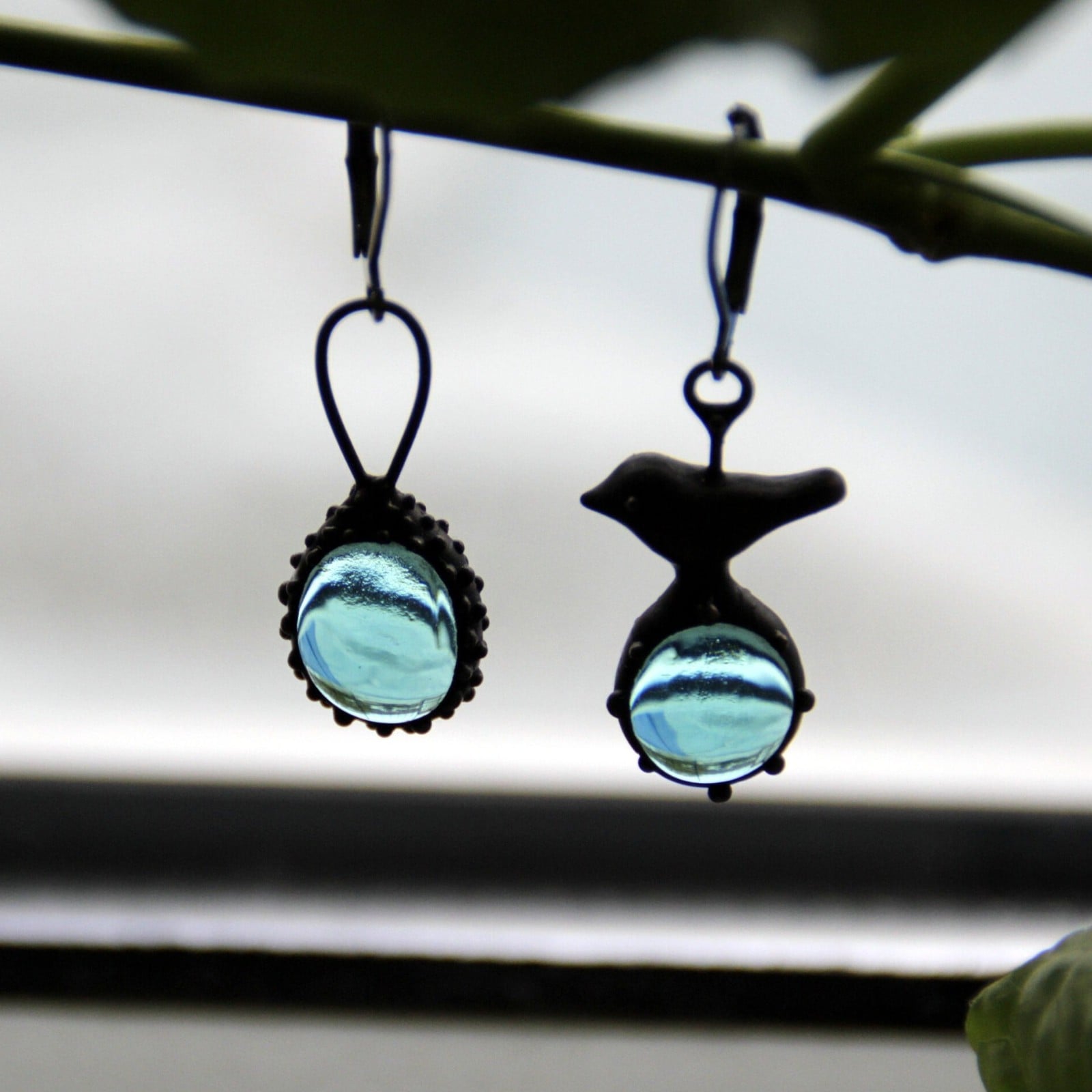 Asymmetrische handgemaakte vogeloorbellen met blauw glas en zwart gepatineerd koper