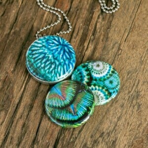 Roestvrij stalen fotomedaillon ketting in teal blauw met drie verschillende verwisselbare voorkanten met close up foto`s in pauw blauw.Pauwenveer close up. Rvs/roesvrij stalen fotomedaillon. Voor het dicht bij je dragen van je favoriete foto.