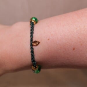 Gevlochten donkergroene armband met gekraakte kralen en goudkleurig blaadje