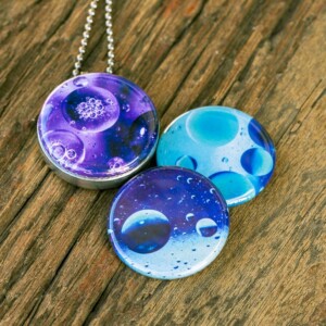 Roestvrij stalen fotomedaillon ketting met drie verschillende verwisselbare voorkanten met close up foto`s van olie druppels in water in ijsblauw, paars en aqua blauwe tinten. Rvs/roesvrij stalen fotomedaillon. Binnenin komt je favoriete foto.