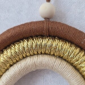 Handgemaakte regenboog hanger (15 × 11 cm) in warme aardetinten. Uniek, lichtgewicht en perfect voor elke kamer