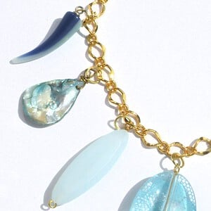 Goudkleurige schakelketting met hangers van schelp, parelmoer, kunsthars en glas. Modieuze halsketting met turquoise bedel, Per Elle ketting