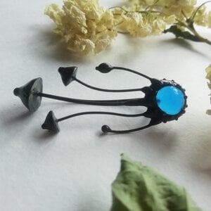 Handgemaakte paddenstoelenbroche met blauw glas en zwart gepatineerd koper