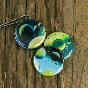 Roestvrij stalen fotomedaillon ketting met drie verschillende verwisselbare voorkanten met close up foto`s van olie druppels in water, het lijken bijna planeten. Rvs/roesvrij stalen fotomedaillon. Voor het dicht bij je dragen van je favoriete foto.