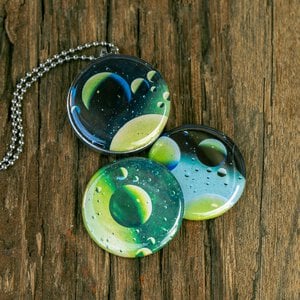 Roestvrij stalen fotomedaillon ketting met drie verschillende verwisselbare voorkanten met close up foto`s van olie druppels in water, het lijken bijna planeten. Rvs/roesvrij stalen fotomedaillon. Voor het dicht bij je dragen van je favoriete foto.