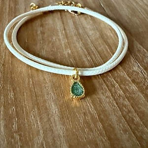Stijlvol armbandje van crèmekleurig polyurethaan leer met een klein groen bedeltje.