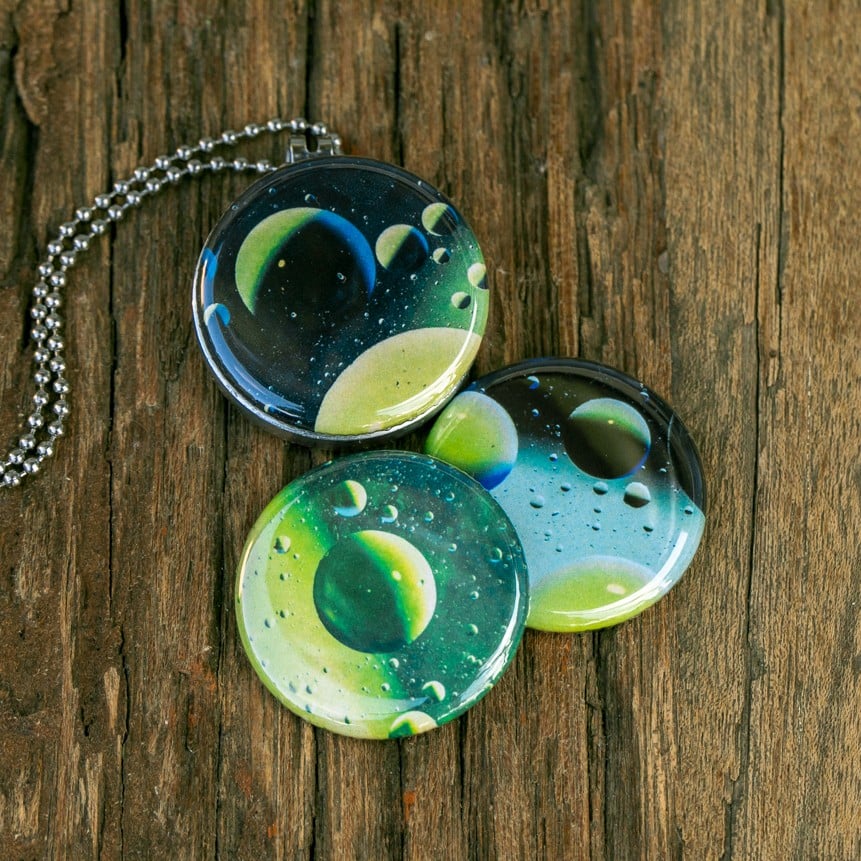 Roestvrij stalen fotomedaillon ketting met drie verschillende verwisselbare voorkanten met close up foto`s van olie druppels in water, het lijken bijna planeten. Rvs/roesvrij stalen fotomedaillon. Voor het dicht bij je dragen van je favoriete foto.