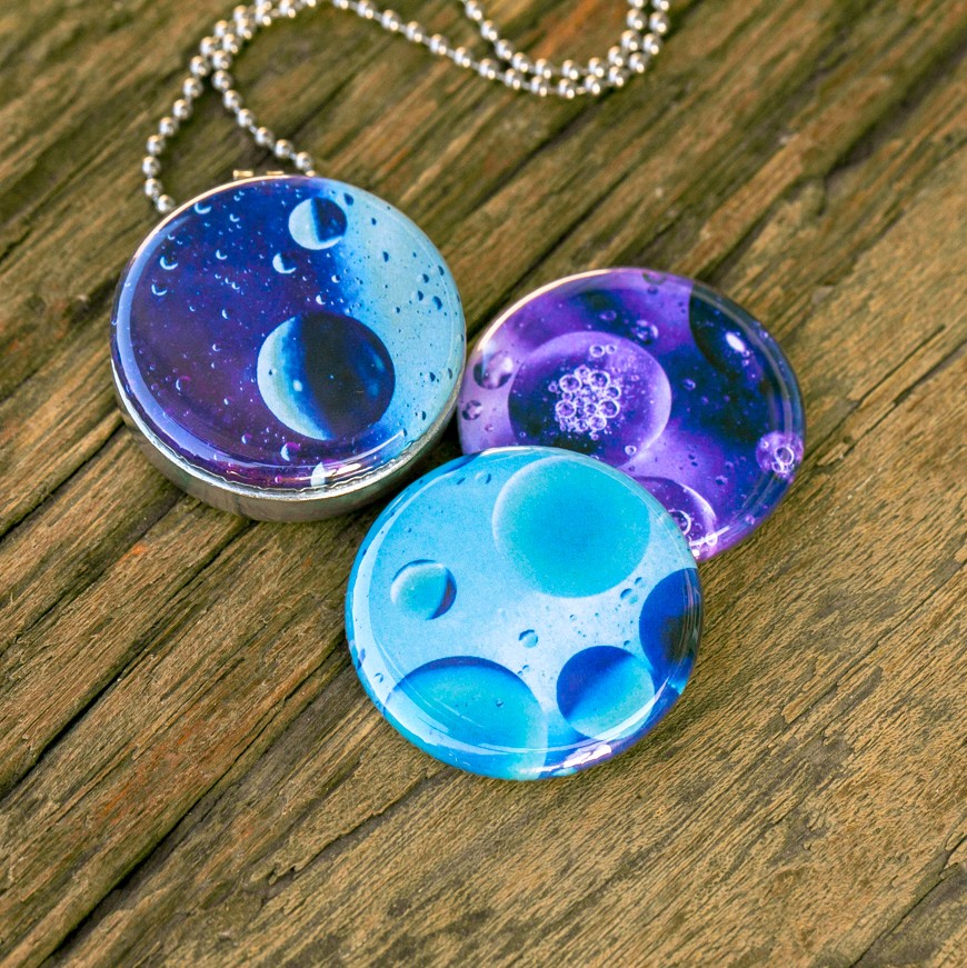 Roestvrij stalen fotomedaillon ketting met drie verschillende verwisselbare voorkanten met close up foto`s van olie druppels in water in ijsblauw, paars en aqua blauwe tinten. Rvs/roesvrij stalen fotomedaillon. Binnenin komt je favoriete foto.