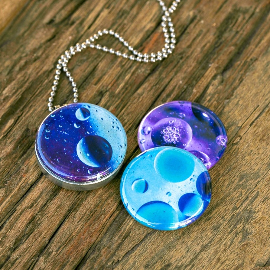 Roestvrij stalen fotomedaillon ketting met drie verschillende verwisselbare voorkanten met close up foto`s van olie druppels in water in ijsblauw, paars en aqua blauwe tinten. Rvs/roesvrij stalen fotomedaillon. Binnenin komt je favoriete foto.